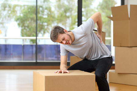 man suffering back ache moving boxes in his new house